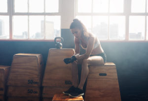 Portrait of tired looking fitness woman sitting on box at gym. She is relaxing after her intense workout.
